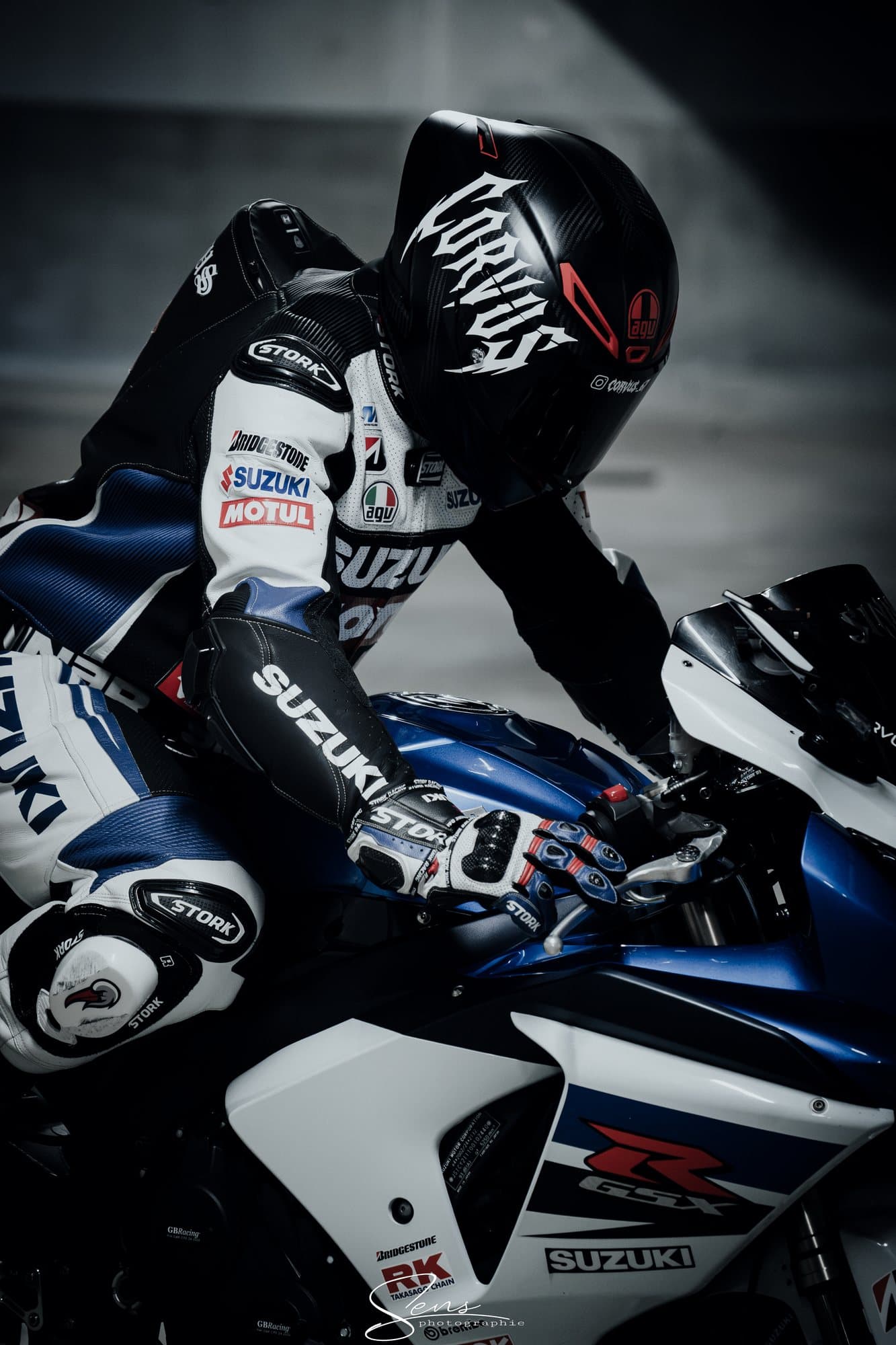 Pilote en combinaison de course penché sur une moto sportive bleue et blanche