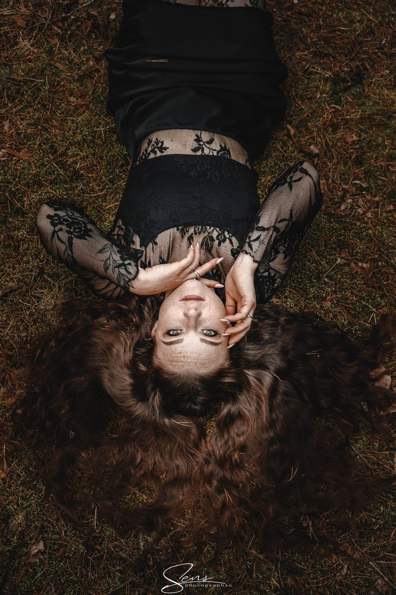 Jeune femme allongée dans l'herbe, cheveux étalés, vêtue de dentelle noire, vue d'en haut